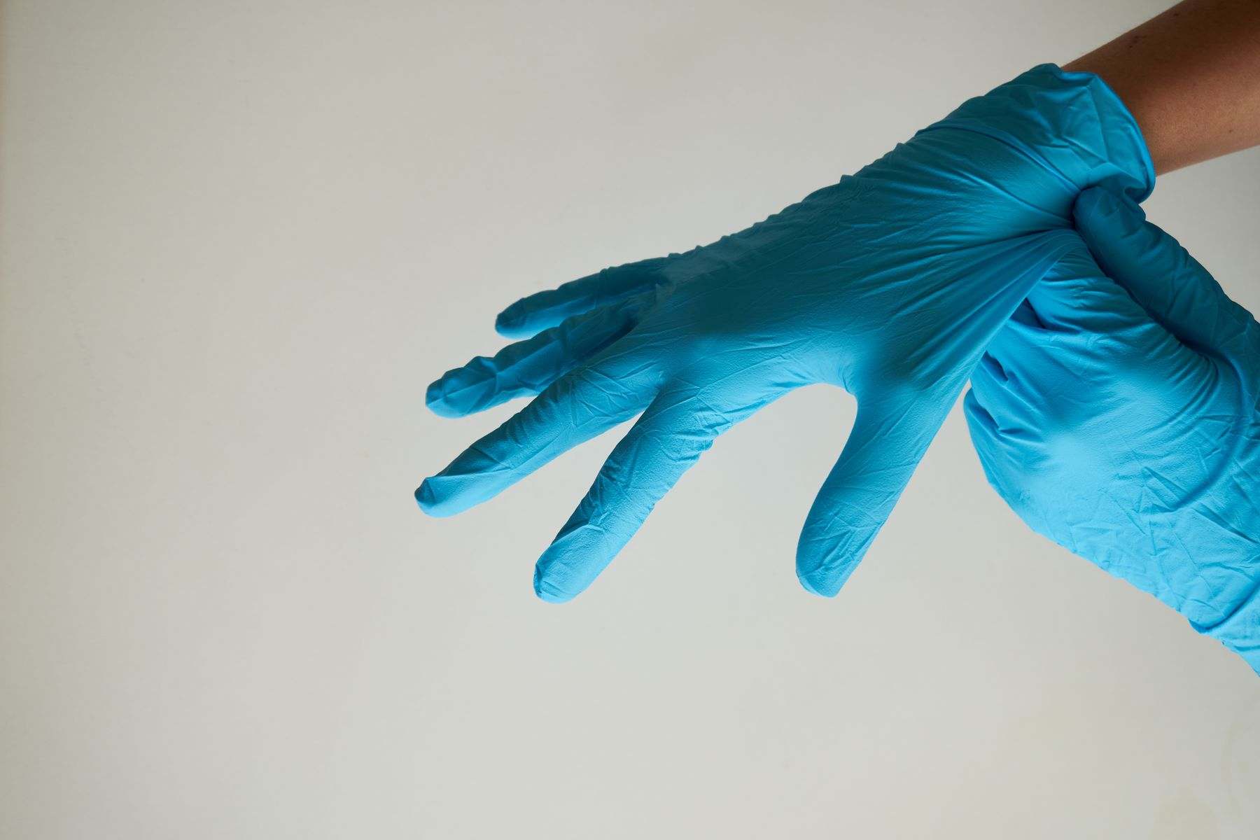 Manos colocándose un guante azul de nitrilo sobre un fondo claro